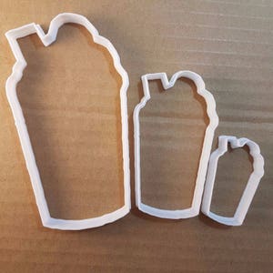 May include: Three white plastic cookie cutters shaped like different sizes of iced coffee drinks. The largest cutter is about 4 inches tall and the smallest is about 2 inches tall.