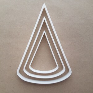 May include: A set of three white plastic triangle cookie cutters. The cutters are nested inside each other, with the largest cutter at the bottom and the smallest cutter at the top.
