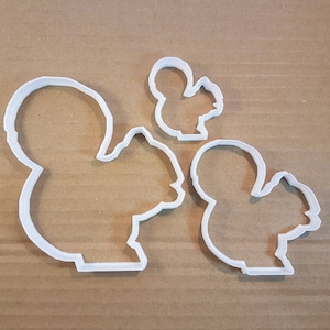 May include: Three white plastic cookie cutters shaped like squirrels. The largest cutter is a full-body squirrel, the medium cutter is a squirrel with its tail curled up, and the smallest cutter is a squirrel with its tail curled up and its head tilted to the side.