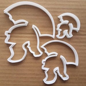 Puede incluir: Conjunto de cinco cortadores de galletas de plástico blanco con forma de cascos romanos. Los cortadores están superpuestos.