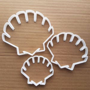 Puede incluir: Tres cortadores de galletas de plástico blanco con forma de conchas. La concha más grande está en la parte superior de la imagen, y la concha más pequeña está en la parte inferior de la imagen.