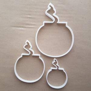 May include: Three white plastic cookie cutters shaped like bombs with a lit fuse. The cutters are different sizes.