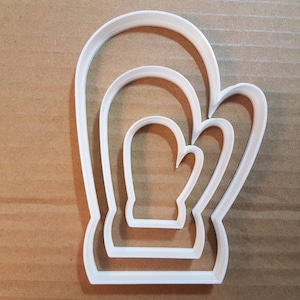 Puede incluir: Un cortador de galletas de plástico blanco con forma de guante. El cortador tiene tres tamaños diferentes, lo que te permite crear guantes de diferentes tamaños.