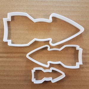 Könnte beinhalten: Drei weiße Plastik-Ausstecher in Form von Raketen, in verschiedenen Größen. Der größte Ausstecher befindet sich oben im Bild, der kleinste unten.