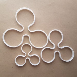May include: Set of six white plastic cookie cutters shaped like a stylized flower with three petals. The cutters are arranged in a cluster on a brown surface.