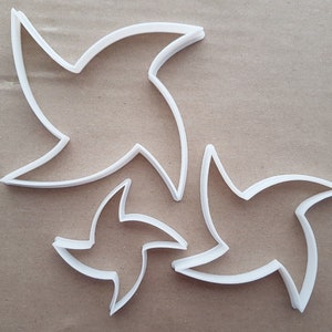 Op de afbeelding: Drie witte plastic koekjesvormen in de vorm van gestileerde sterren. De grootste ster bevindt zich op de achtergrond, met een kleinere ster ervoor en de kleinste ster op de voorgrond.