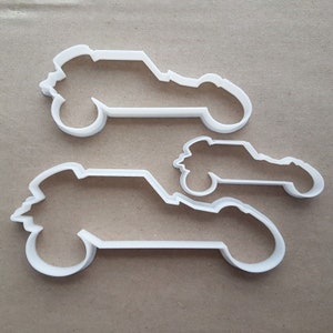 May include: Two white plastic cookie cutters shaped like dune buggies. The larger cutter is in the background and the smaller cutter is in the foreground.