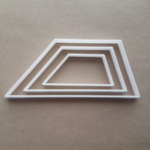 May include: Four white plastic kite-shaped cookie cutters nested together. The cutters are arranged in descending order of size. The largest cutter is at the bottom. The cutters are on a light brown surface.