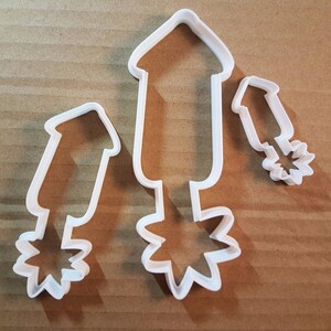 May include: Three white plastic cookie cutters shaped like fireworks. The largest cutter has a starburst at the bottom. The medium cutter has a starburst at the bottom. The smallest cutter has a starburst at the top.