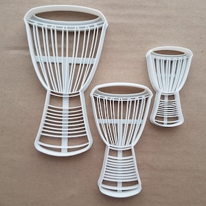 May include: Three white plastic cookie cutters shaped like djembe drums. The largest cutter is 4.5 inches tall and the smallest cutter is 2.5 inches tall.