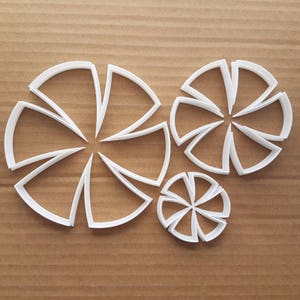 Op de afbeelding: Een set van drie witte plastic koekjesvormen in de vorm van windmolens. De vormen zijn in verschillende maten, met de grootste vorm in het midden en de kleinste vorm rechts.