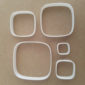 May include: Set of five white plastic cookie cutters shaped like rounded rectangles. The cutters are arranged in a row, with the largest cutter on the left and the smallest cutter on the right.