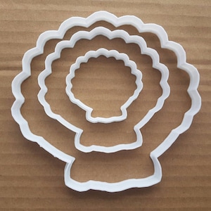 Puede incluir: Cortador de galletas de plástico blanco en forma de concha con tres capas. El cortador está diseñado para crear una forma de concha en capas.