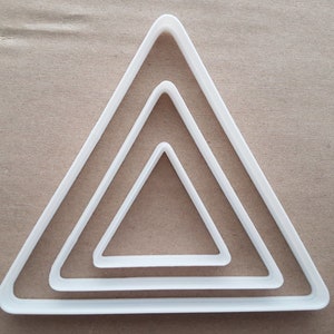 May include: Set of three white plastic triangle cookie cutters. The cutters are nested inside each other, with the largest cutter on the outside and the smallest cutter on the inside.