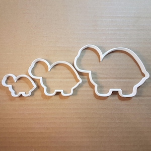 Może przedstawiać: Trzy białe plastikowe foremki do ciasteczek w kształcie żółwia w różnych rozmiarach. Największy żółw jest po prawej stronie, średniej wielkości żółw jest pośrodku, a najmniejszy żółw jest po lewej stronie.