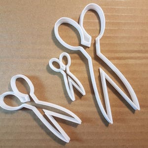 Könnte beinhalten: Drei weiße Plastik-Ausstecher in Form von Scheren in verschiedenen Größen.