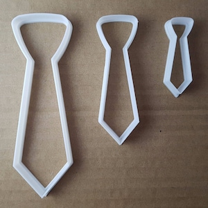 May include: Three white plastic tie-shaped cookie cutters of different sizes.