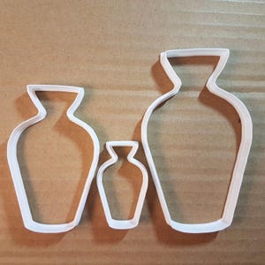 May include: Three white plastic cookie cutters shaped like vases. The largest vase is on the right, the medium vase is on the left, and the smallest vase is in the centre.