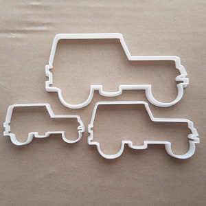 Może przedstawiać: Dwa białe plastikowe wykrawacze do ciasteczek w kształcie jeepa. Większy wykrawacz ma około 12,5 cm długości, a mniejszy około 7,5 cm długości.