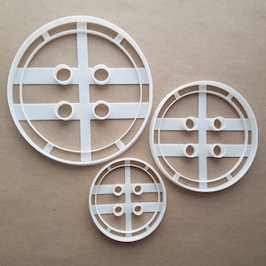 Peut inclure: Trois emportes-pièces en plastique blanc en forme de boutons de différentes tailles. Le plus grand emporte-pièce a quatre trous et un bord surélevé. L'emporte-pièce moyen a quatre trous. Le plus petit emporte-pièce a quatre trous.