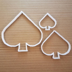 Puede incluir: Tres cortadores de galletas de plástico blanco en forma de picas de diferentes tamaños. El cortador más grande mide aproximadamente 12,5 cm de alto y el más pequeño aproximadamente 5 cm de alto.