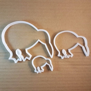 May include: Three white plastic cookie cutters shaped like kiwis, in different sizes. The largest cutter is at the back, the medium cutter is in the middle, and the smallest cutter is at the front.