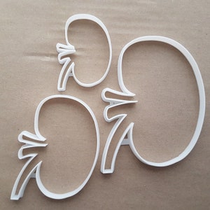 May include: Three white plastic cookie cutters shaped like kidneys. The cutters are different sizes.