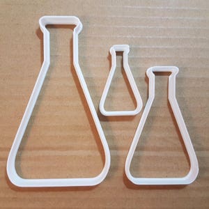 Könnte beinhalten: Drei weiße Plastik-Ausstecher in Form von Bechergläsern. Das größte Becherglas ist etwa 12,5 cm hoch, das mittlere Becherglas ist etwa 7,5 cm hoch und das kleinste Becherglas ist etwa 5 cm hoch.