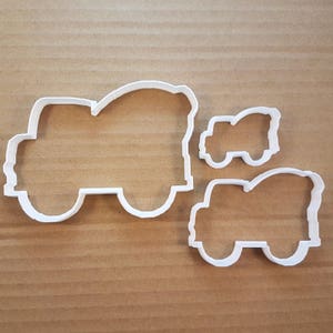 Peut inclure: Trois emporte-pièces en plastique blanc en forme de camions. Le plus grand camion a une bétonnière à l'arrière. Le plus petit camion est une dépanneuse.