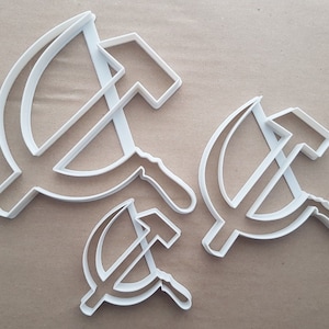 May include: Three white plastic cookie cutters in the shape of a hammer and sickle, a symbol of communism. The cutters are of different sizes.