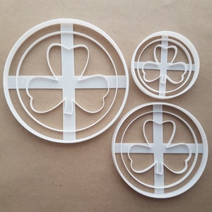 May include: Three white plastic cookie cutters shaped like a four-leaf clover. The cutters are in different sizes.