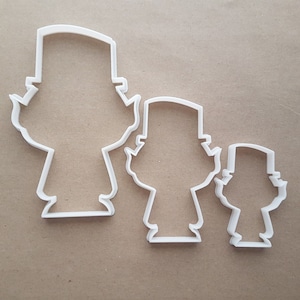 Może przedstawiać: Trzy białe plastikowe foremki do ciasteczek w kształcie kreskówkowych postaci w kapeluszach. Formy są w różnych rozmiarach, największa po lewej, a najmniejsza po prawej.