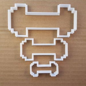以下が含まれることがあります： ピクセル化されたビデオゲームキャラクターの形をした、白いプラスチック製のクッキーカッター4個セット。カッターは積み重ねられており、一番大きなカッターが下、一番小さなカッターが上にあります。