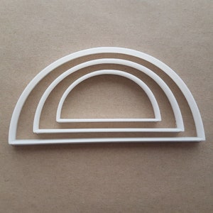 Könnte beinhalten: Drei weiße, halbkreisförmige Ausstecher aus Kunststoff in verschiedenen Größen, übereinander gestapelt. Der größte Ausstecher befindet sich unten, der kleinste oben.