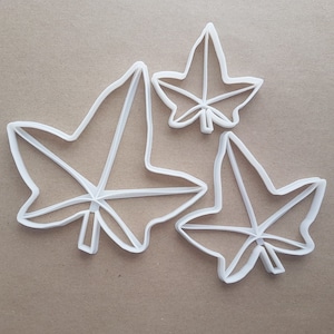 May include: Three white plastic cookie cutters shaped like ivy leaves. The cutters are different sizes.