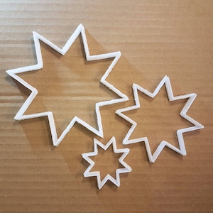 May include: Three white plastic star-shaped cookie cutters of different sizes. The largest cutter is at the top left of the image, the medium-sized cutter is to the right of the largest cutter, and the smallest cutter is at the bottom centre of the image.
