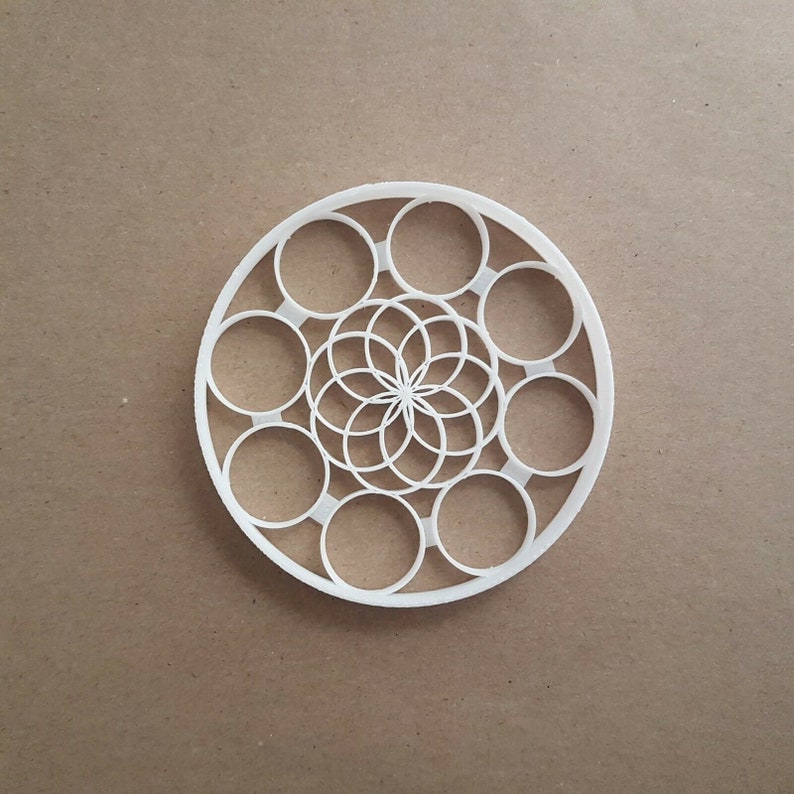 May include: White circular mandala design with a flower in the center and a ring of circles around it.