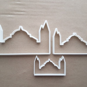 Op de afbeelding: Drie witte plastic koekjesvormen in de vorm van de skyline van een stad met koepelvormige gebouwen.