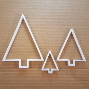 May include: Three white plastic Christmas tree cookie cutters of different sizes. The largest cutter is on the left, the medium cutter is on the right, and the smallest cutter is in the centre.