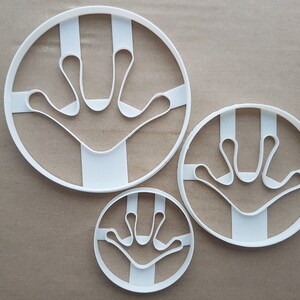 Peut inclure: Trois emportes-pièces en plastique blanc de différentes tailles, chacun présentant un motif d'empreinte de main avec trois doigts et un pouce.