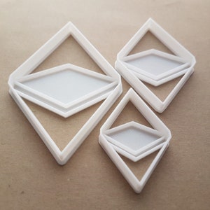 May include: Three white plastic cookie cutters shaped like the Ethereum cryptocurrency logo. The cutters are different sizes, with the largest cutter being in the center of the image.