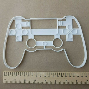 May include: White plastic cookie cutter shaped like a video game controller. The cutter is approximately 20 cm wide.