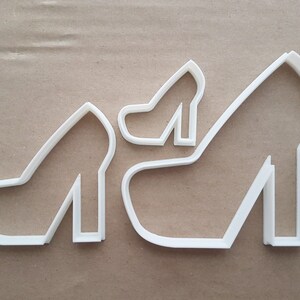 May include: Two white plastic cookie cutters shaped like high-heeled shoes. The larger shoe cutter is about 10 cm tall and the smaller shoe cutter is about 5 cm tall.