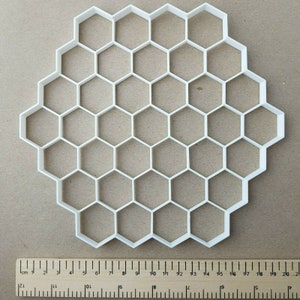 May include: White plastic honeycomb mold with 21 hexagonal cavities. The mold is approximately 18 cm in diameter.