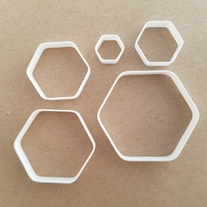 Puede incluir: Conjunto de cinco cortadores de galletas hexagonales de plástico blanco de diferentes tamaños.