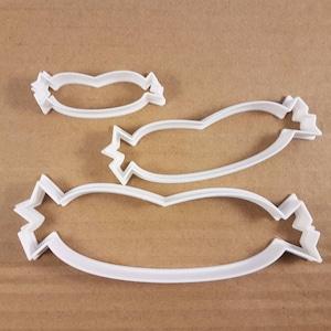 May include: Three white plastic cookie cutters shaped like different sizes of sausages.