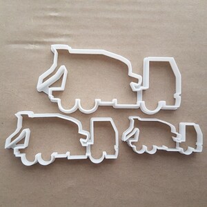 Può includere: Un set di quattro stampini per biscotti in plastica bianca a forma di camion con cassone ribaltabile. Lo stampino più grande è al centro dell'immagine, con tre stampini più piccoli sotto.