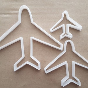 以下が含まれることがあります： 3つの異なるサイズの白いプラスチック製の飛行機型クッキーカッター。一番大きいカッターは背景に、中くらいのカッターは中央に、一番小さいカッターは前景にあります。