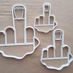 May include: Three white plastic cookie cutters shaped like middle fingers. The cutters are different sizes.