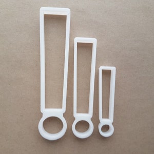 Könnte beinhalten: Drei weiße Plastik-Ausstecher in Form von Ausrufezeichen in verschiedenen Größen.